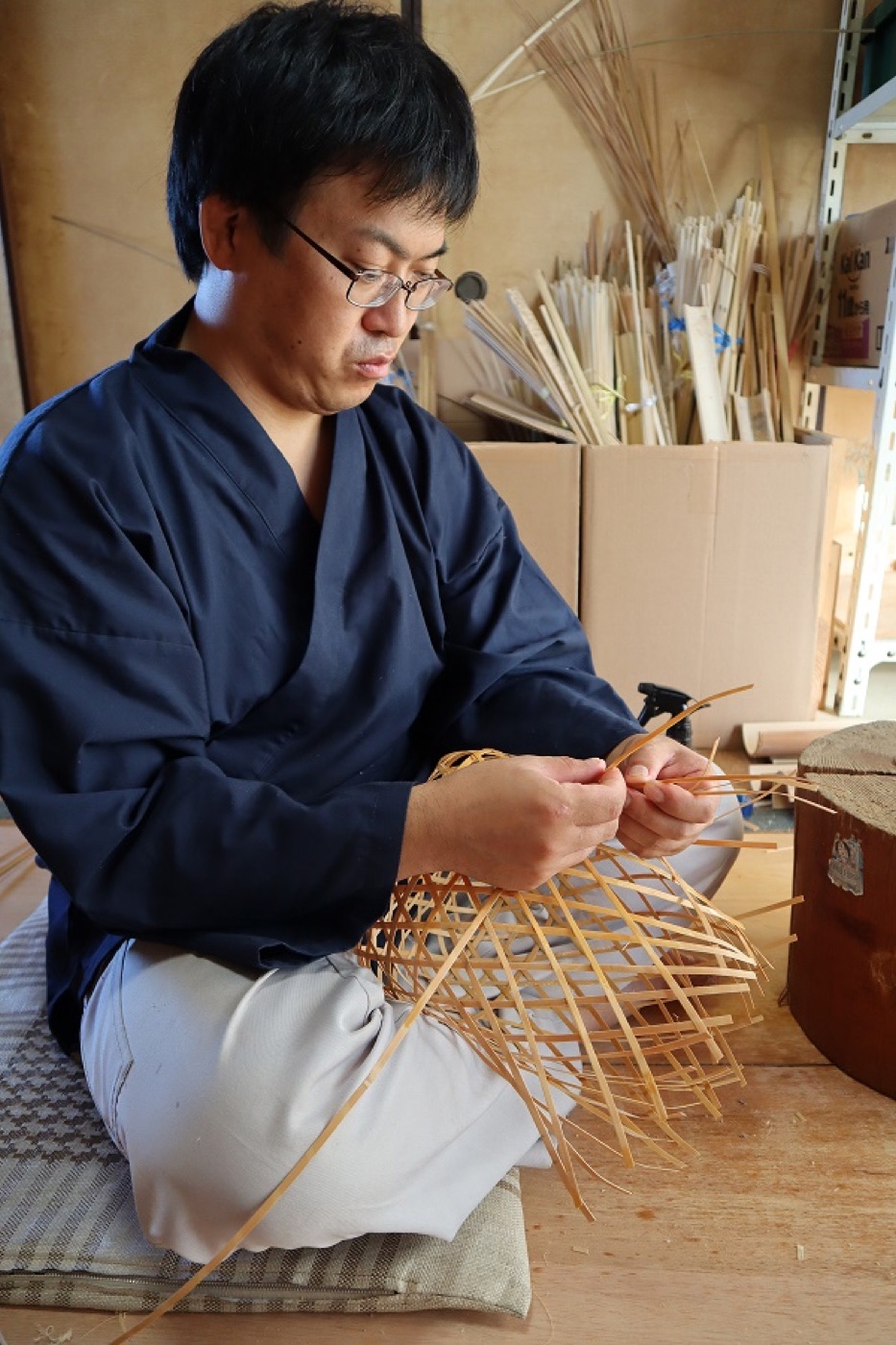 紺の作務衣姿で竹かごを編む三沢俊一氏